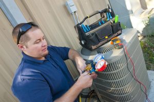 technician with tools and tool bag inspecting the outside unit of an air conditioner