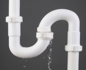 Closeup of a sink S Trap made of white PVC plastic with a broken connection and water pouring out. Square format over a gray background.