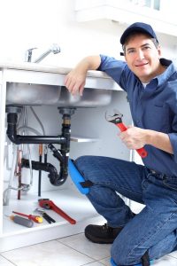 plumber working on plumbing system under sink