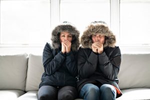 couple-sitting-on-couch-shivering-in-jackets