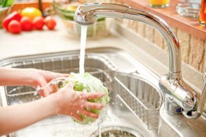 hands-washing-head-of-lettuce-over-drain-in-kitchen-sink