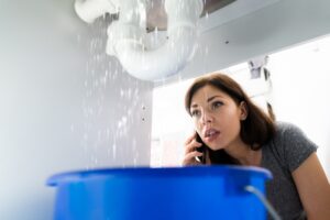 pipe-leaking-water-and-homeowner-looking-at-it-while-on-phone