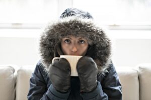 person-in-coat-and-mittens-indoors-sipping-hot-tea